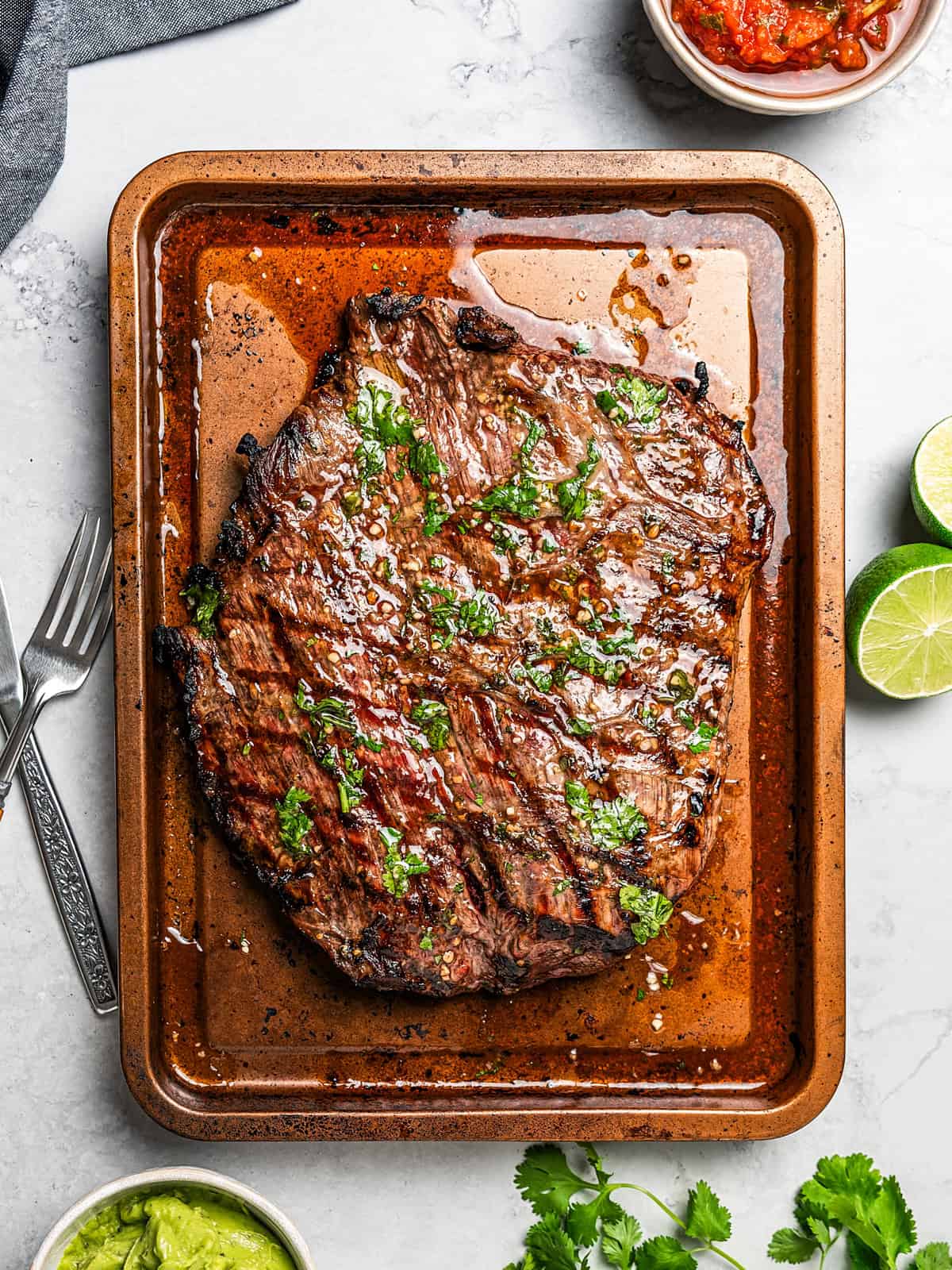 A whole grilled flank steak set on a rimmed baking sheet.