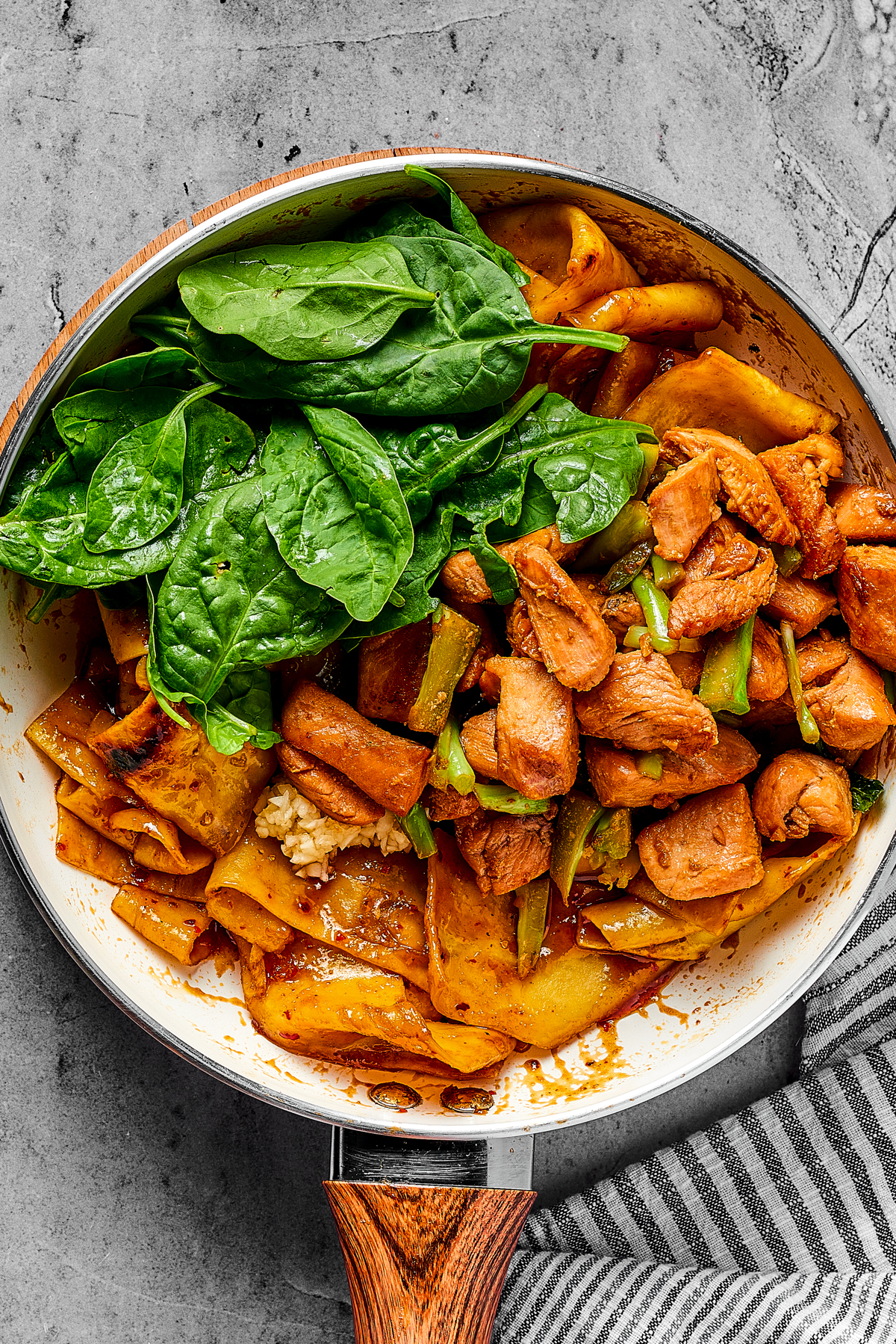 A skillet of noodles and chicken with fresh spinach added.