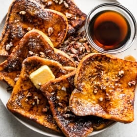 overhead shot of pumpkin french toast slices arranged on a plate with a bowl of maple syrup set next to them.