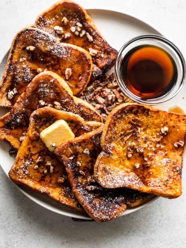 overhead shot of pumpkin french toast slices arranged on a plate with a bowl of maple syrup set next to them.