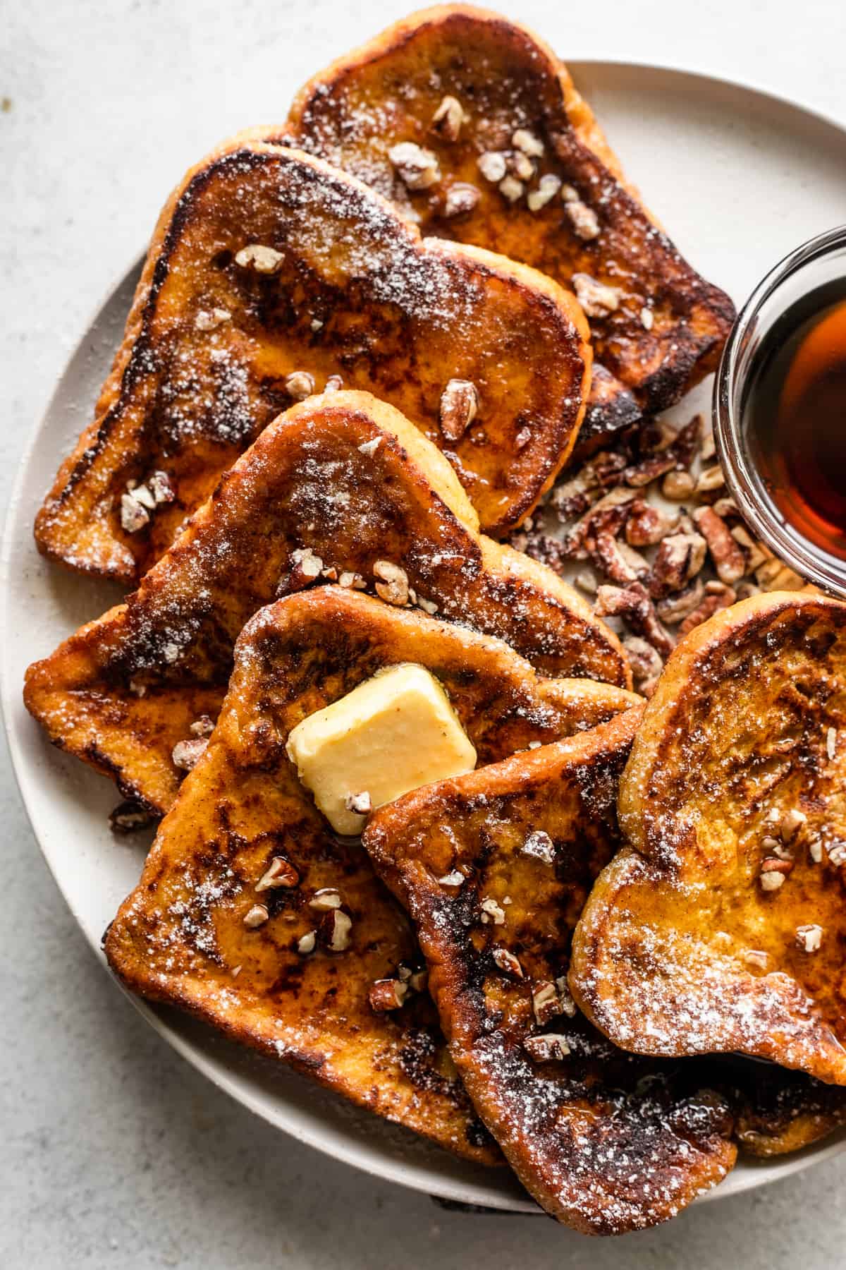 close up overhead shot of pumpkin french toast slices arranged on a plate with a bowl of maple syrup set next to them.