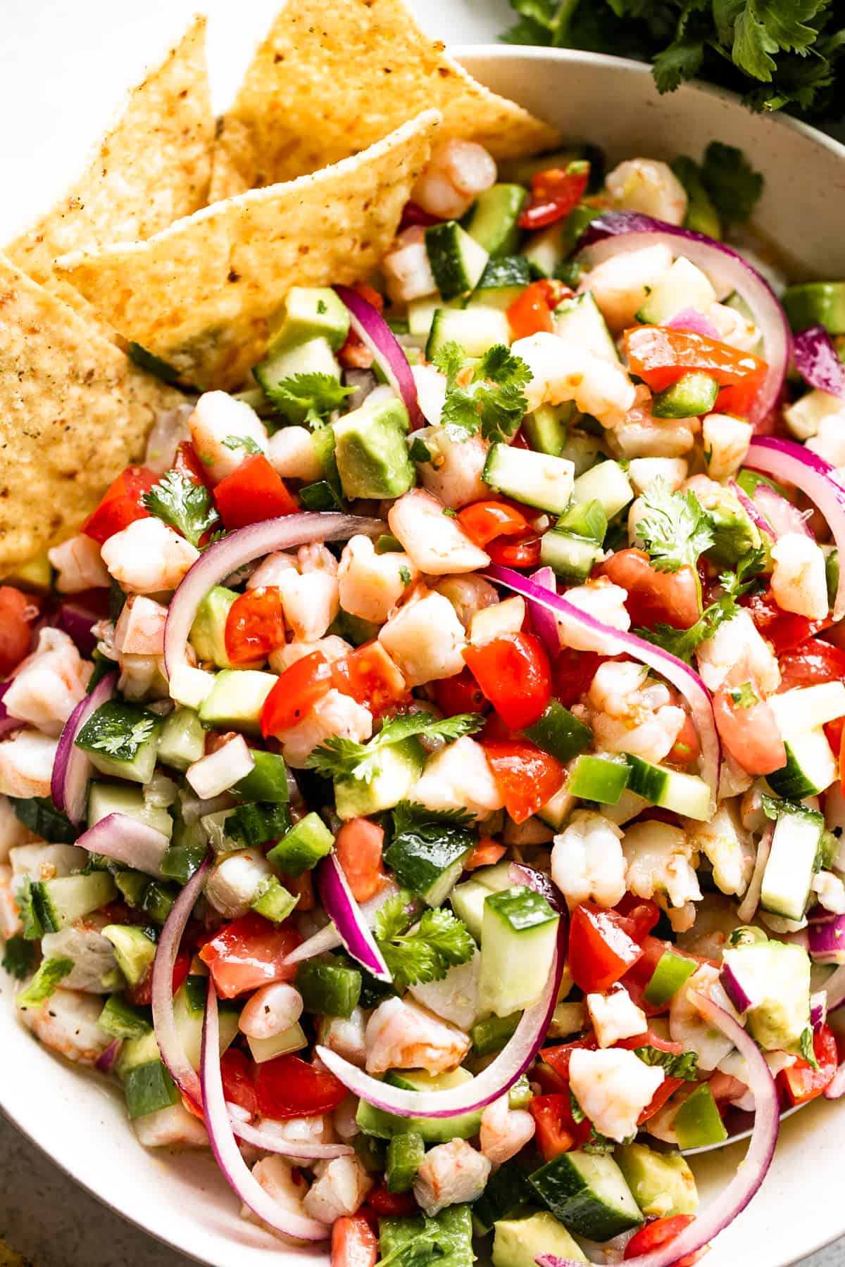 up close shot of shrimp ceviche served in a bowl with four tortilla chips placed on the upper left hand side of the bowl.