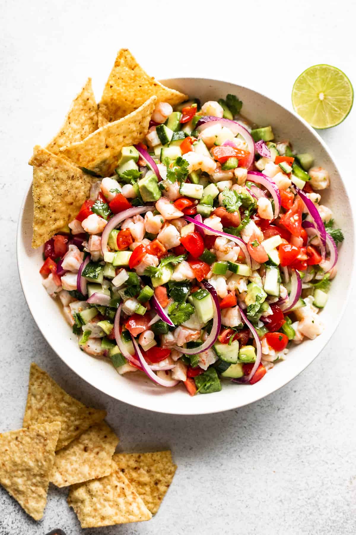 up close shot of shrimp ceviche served in a white bowl with four tortilla chips placed on the upper left hand side of the bowl, and on the bottom left hand side of the bowl.