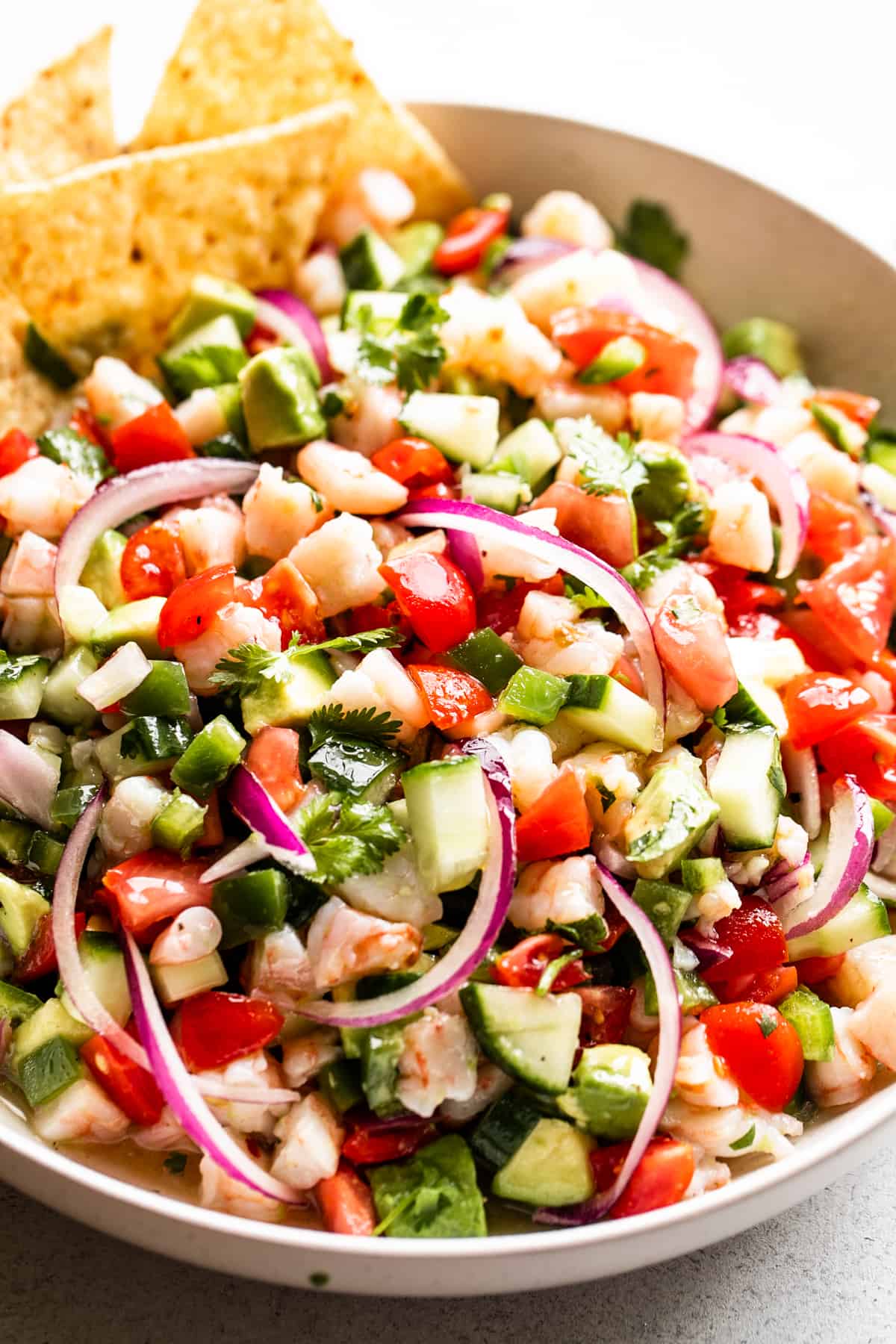 up close shot of shrimp ceviche served in a bowl with four tortilla chips placed on the upper left hand side of the bowl.