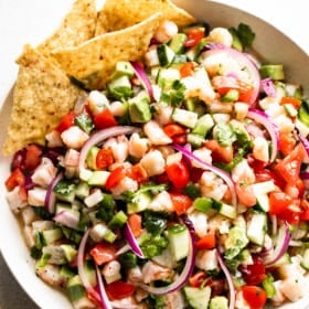 overhead shot of a white bowl with shrimp ceviche that includes diced tomatoes, diced avocado, diced shrimp, diced cucumbers, red onions, and jalapenos.