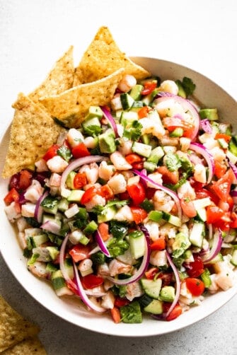overhead shot of a white bowl with shrimp ceviche that includes diced tomatoes, diced avocado, diced shrimp, diced cucumbers, red onions, and jalapenos.