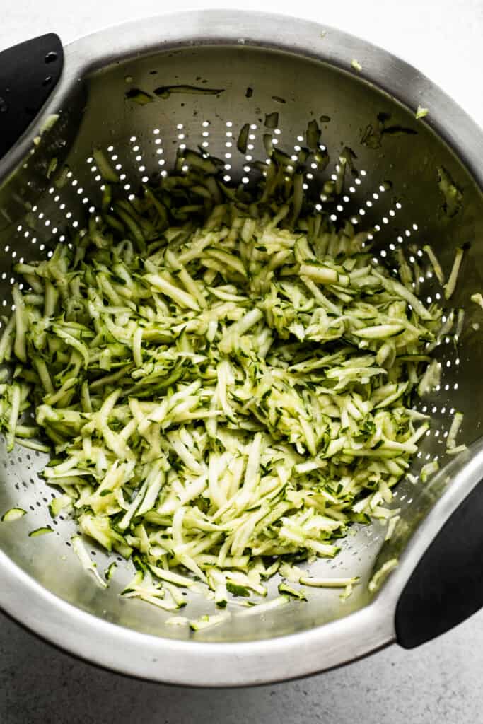 overhead view of a shredded zucchini in a silver colored colander.