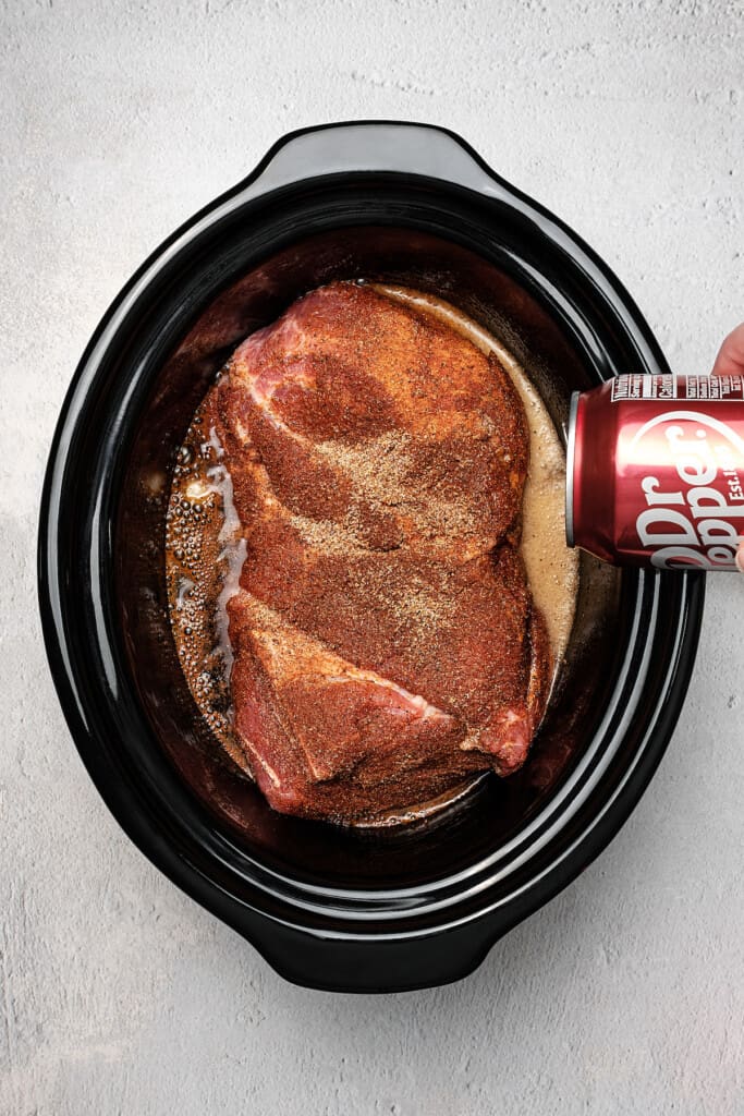Overhead shot of Dr. Pepper being poured into a crock pot with a pork roast.