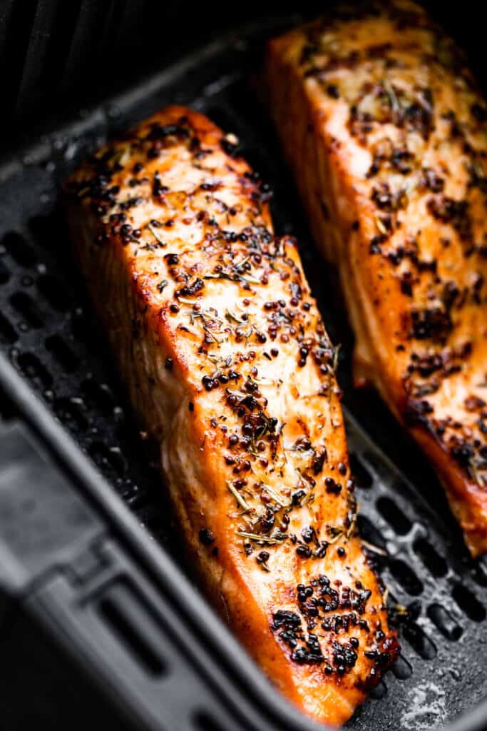 two seasoned salmon fillets in a black air fryer basket.