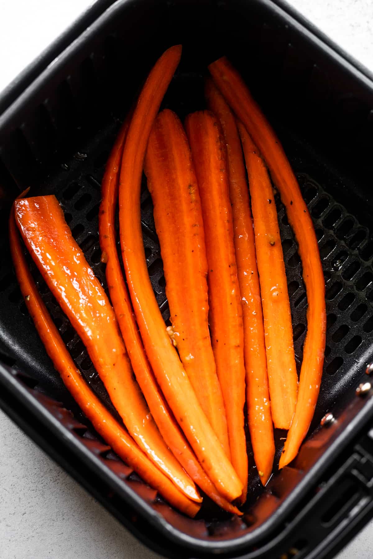 Long carrots in a black air fryer basket.