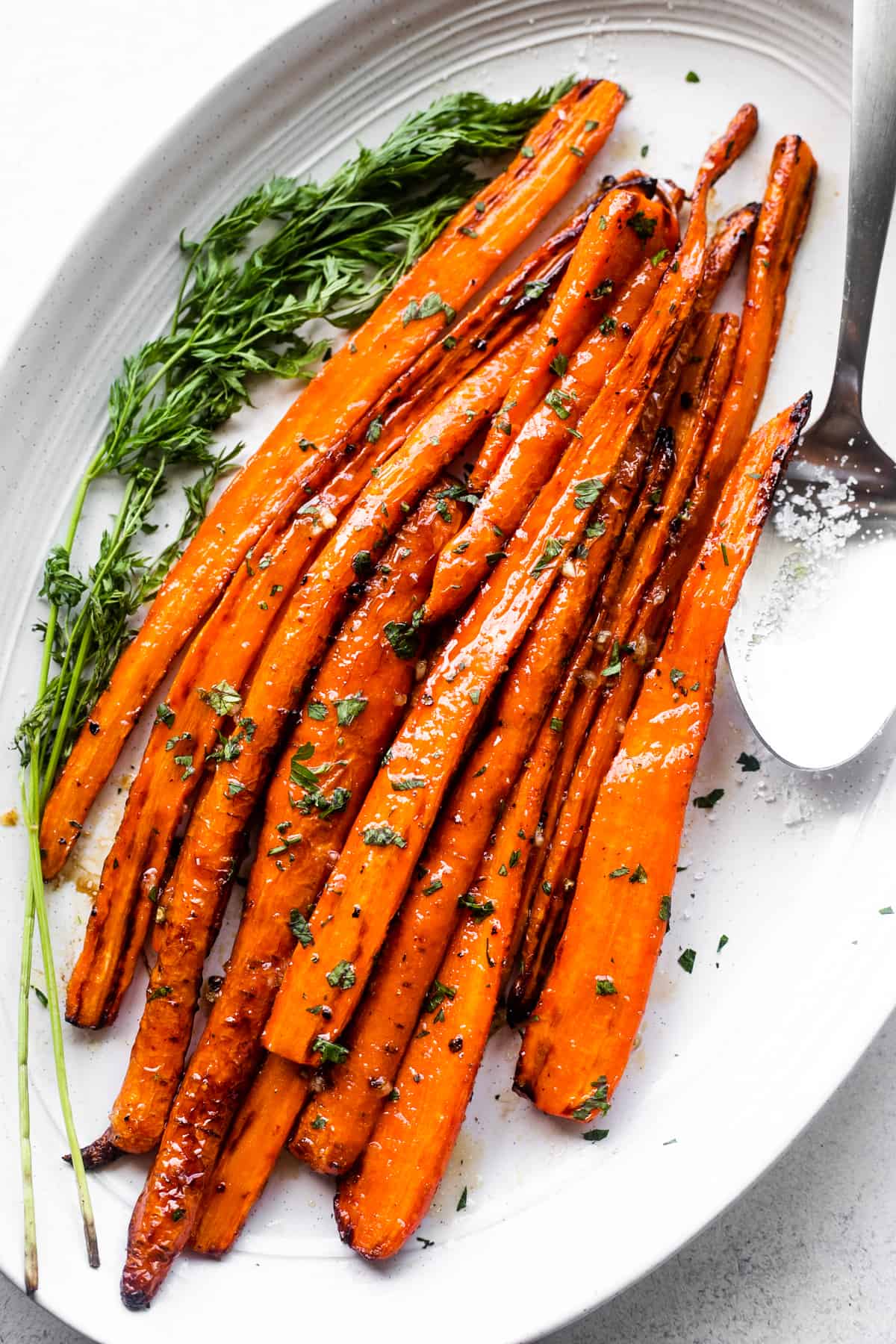 air fryer cooked carrots arranged on a long oblong platter, with a big spoon placed next to the carrots