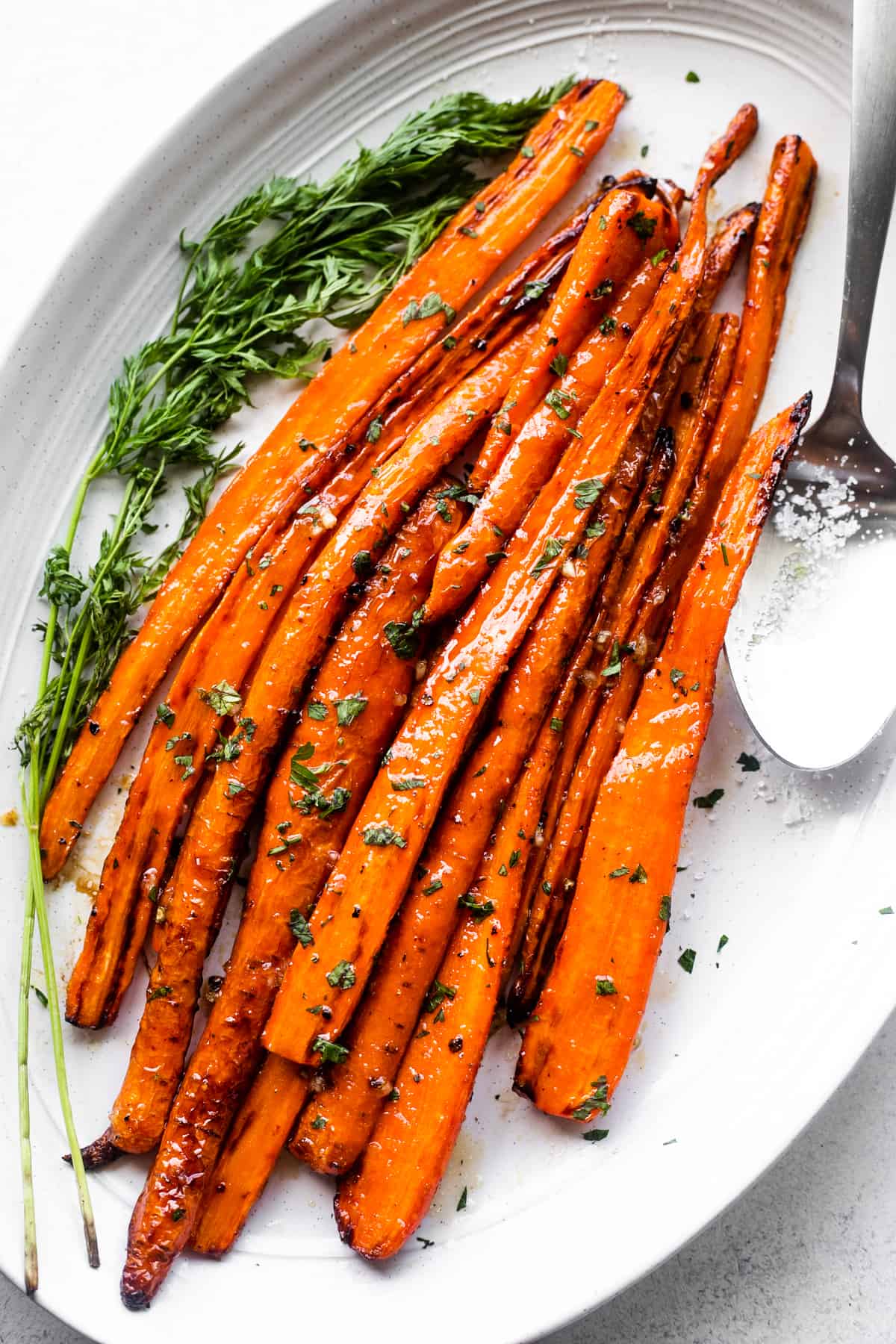 Air fryer cooked carrots arranged on a long oblong platter, with a big spoon placed next to the carrots