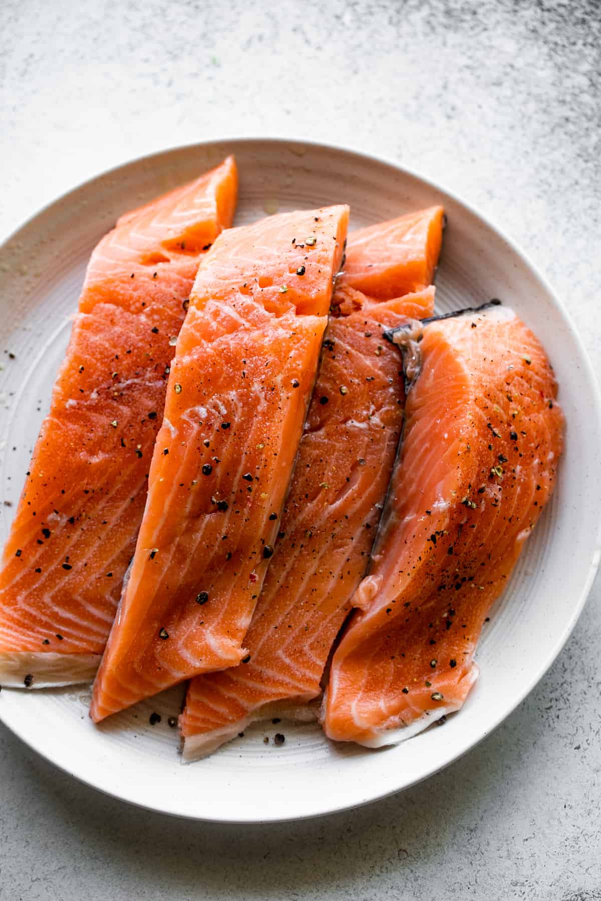 four raw salmon fillets arranged on a white dinner plate.