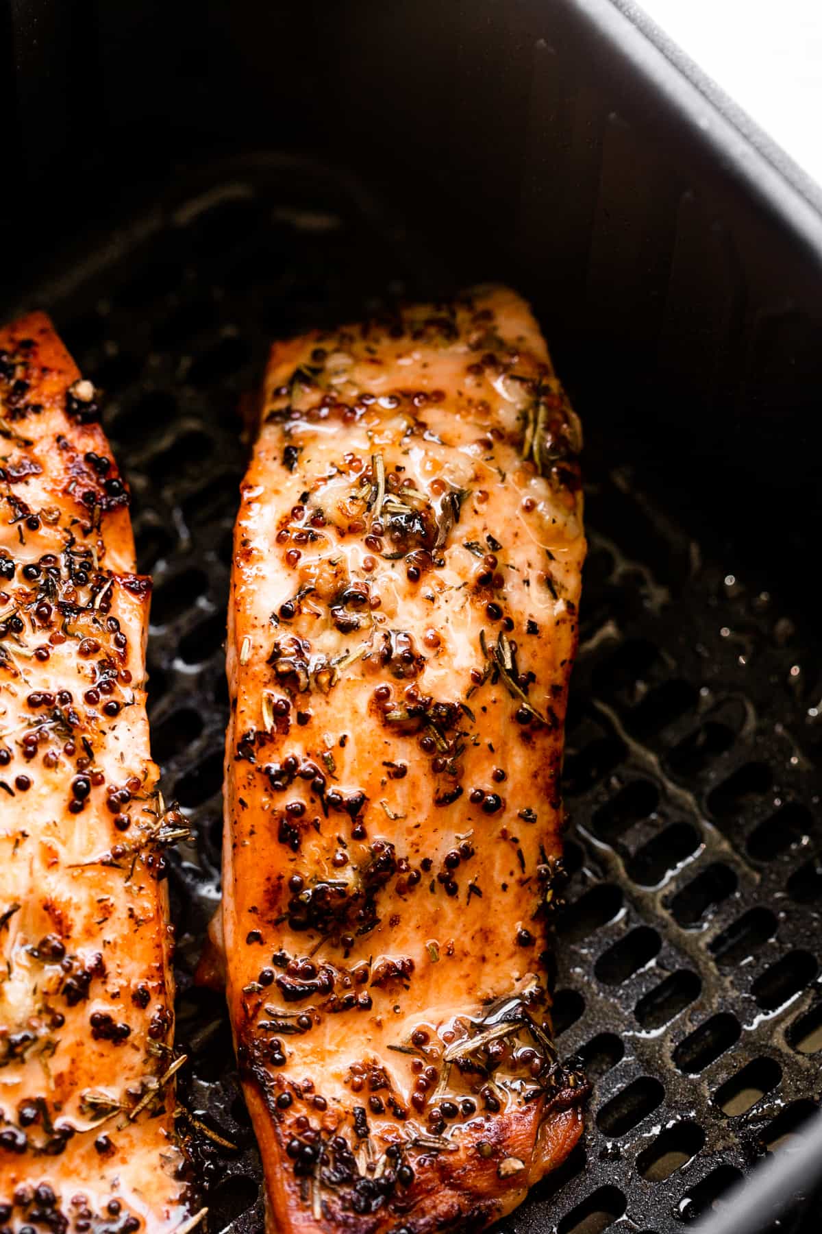 two seasoned salmon fillets in a black air fryer basket.