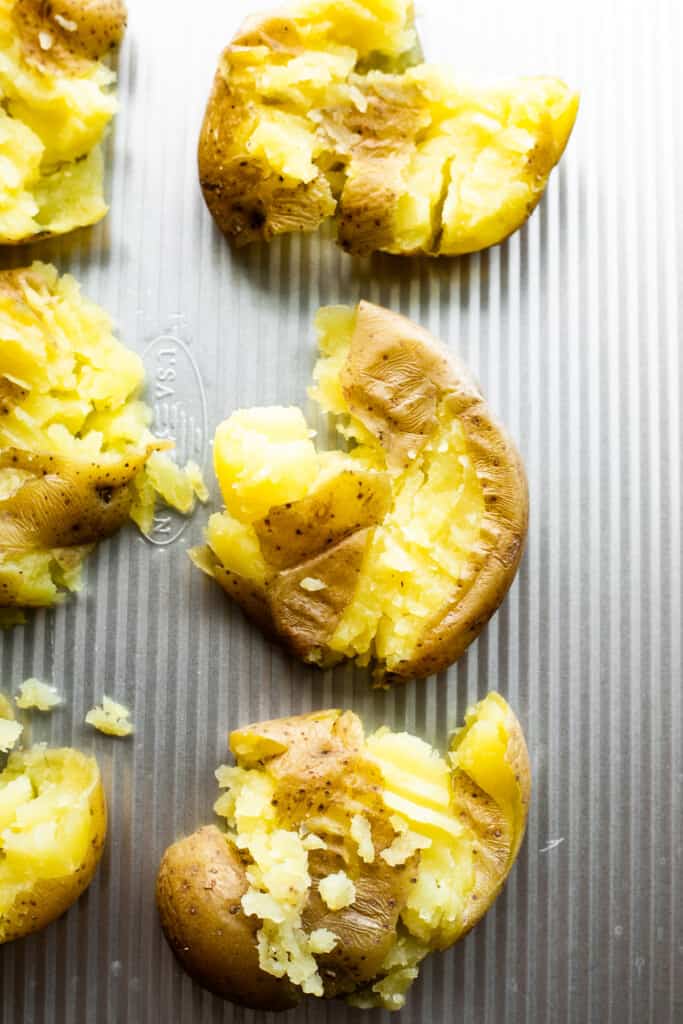 six smashed potatoes arranged on a silver colored background