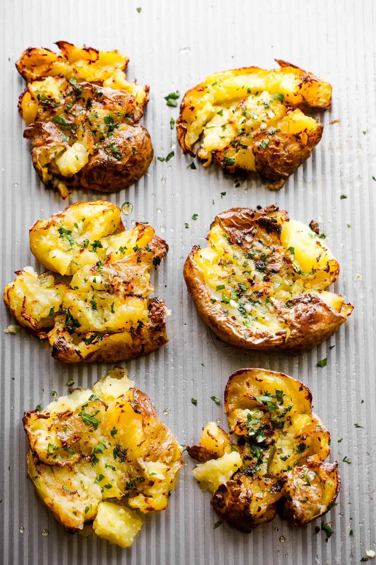 six smashed potatoes arranged on a silver colored backdrop