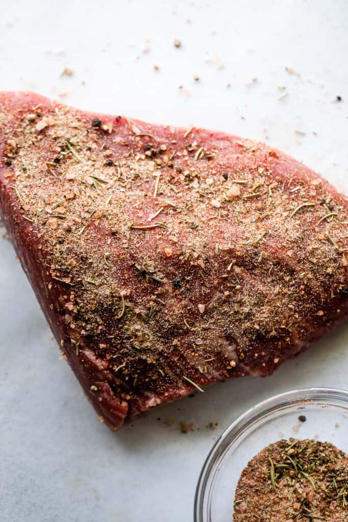 raw piece of tri tip with seasoning sprinkled all over the top.
