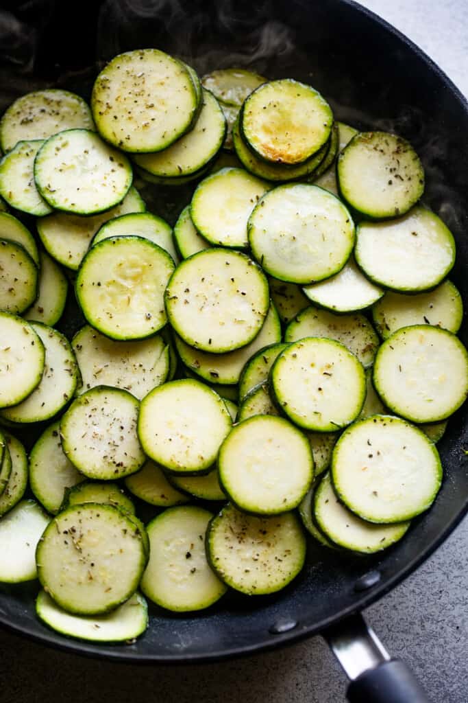 round zucchini slices cooking in a black skillet.
