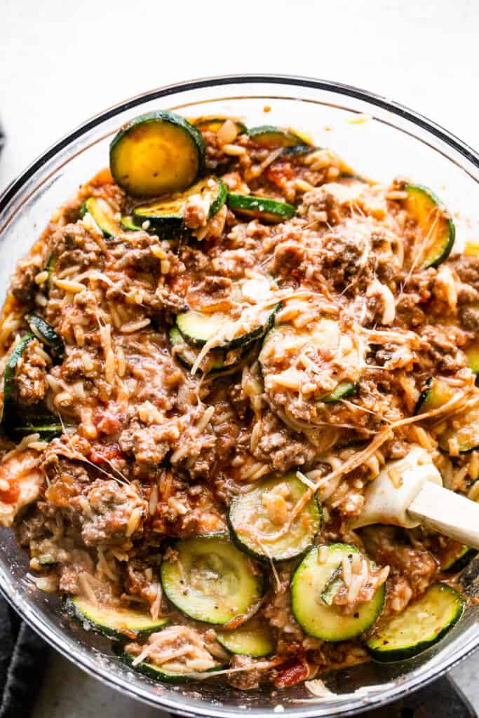 stirring together cooked ground beef and slices of zucchini in a big glass mixing bowl.