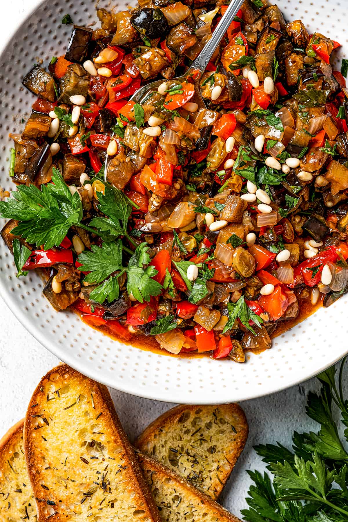 A white bowl of caponata with baguette slices.