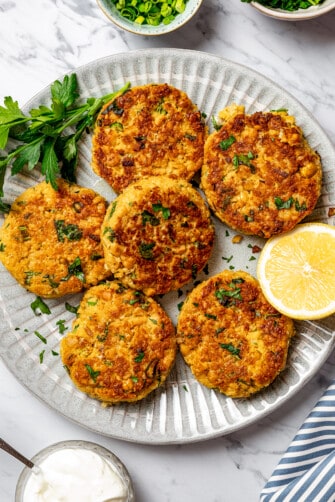 Garbanzo bean patties on a plate, garnished with herbs and lemon.