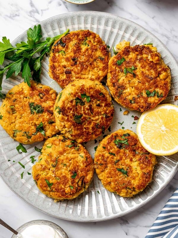 Garbanzo bean patties on a plate, garnished with herbs and lemon.