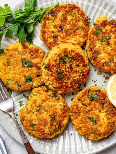 Six chickpea patties on a serving platter, garnished with parsley and lemon.