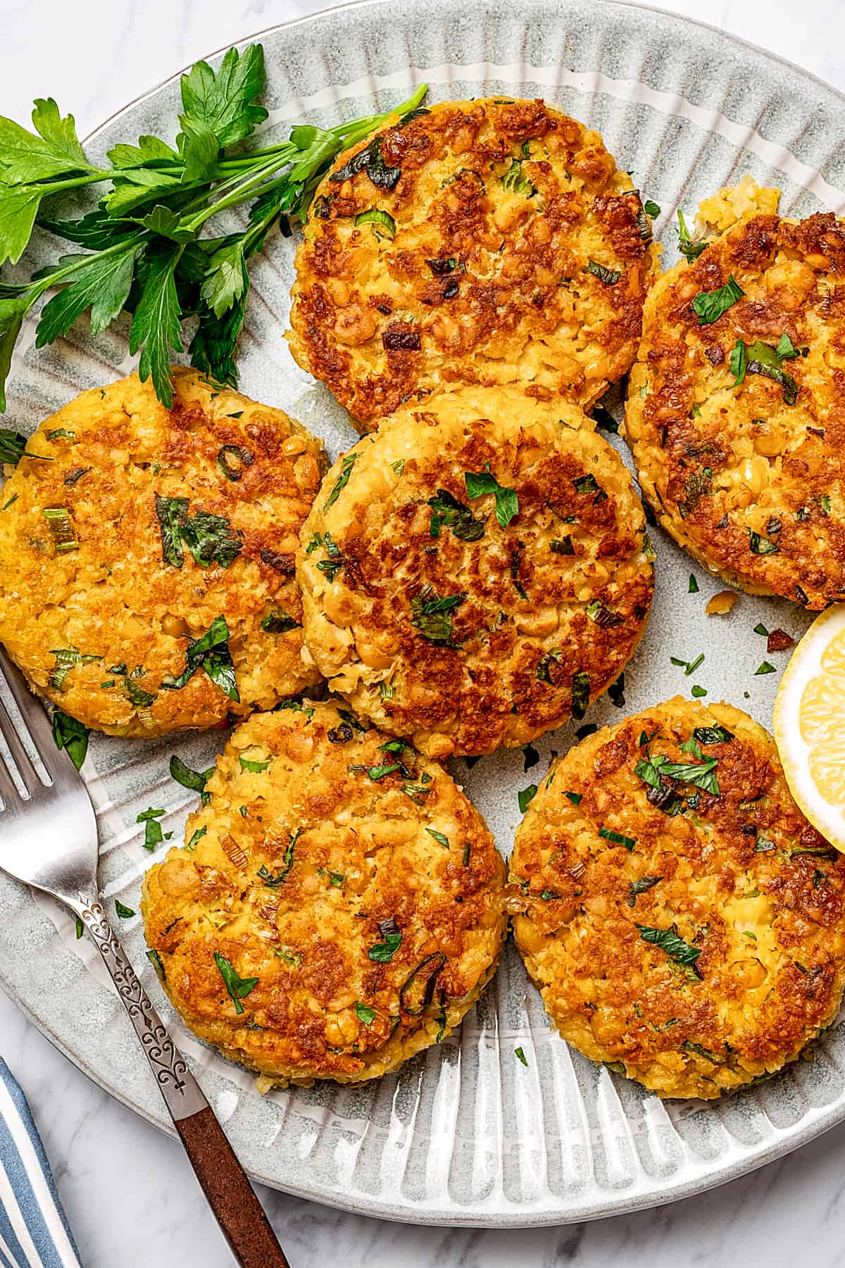 Six chickpea patties on a serving platter, garnished with parsley and lemon.