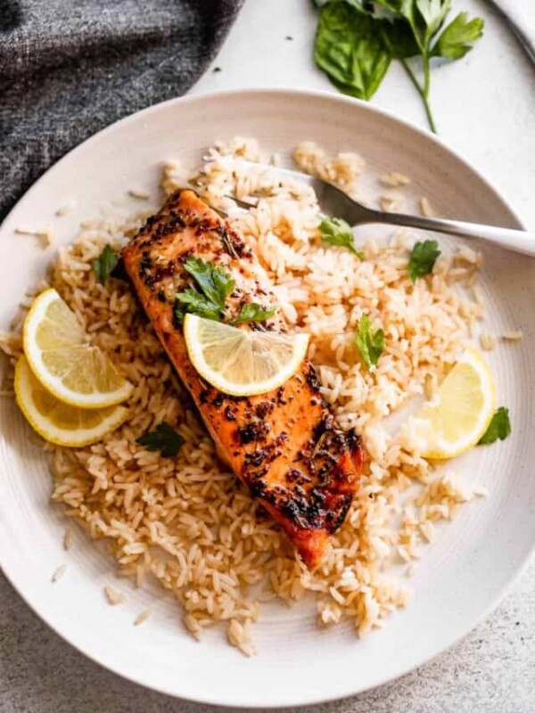 dinner plate with air fryer salmon fillet set atop a bed of rice and topped with lemon slices.