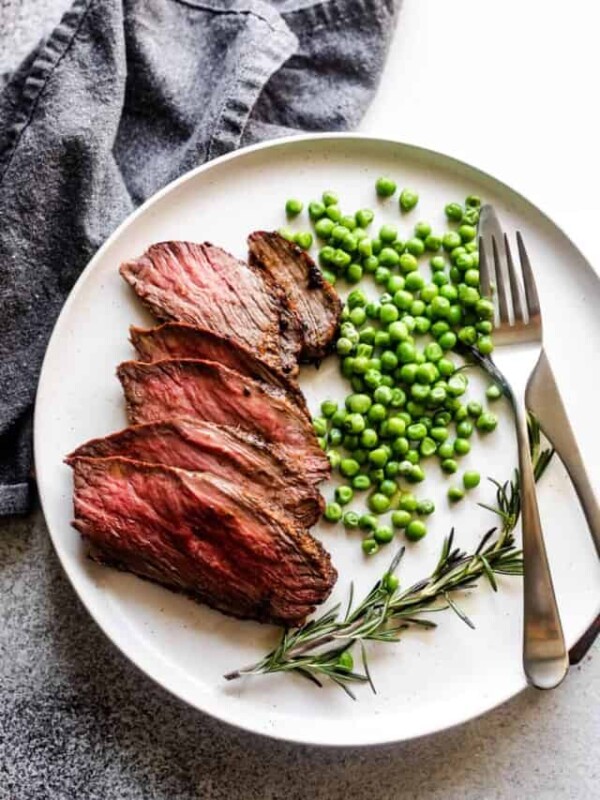 slices of sirloin tip roast arranged on a plate with green peas and a rosemary branch served next to it.