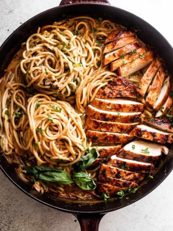 overhead shot of a cast iron skillet with two nests of zoodles arranged on the left side, and sliced chicken breasts arranged on the right side of the skillet.