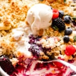 up close shot of a spoon scooping out berry cobbler, with a scoop of ice cream placed right above the spoon.