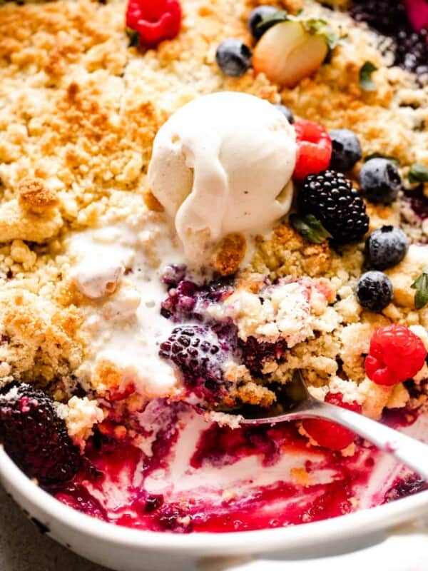 up close shot of a spoon scooping out berry cobbler, with a scoop of ice cream placed right above the spoon.