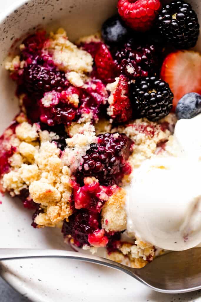 close up shot of a berry cobbler served in a white bowl with vanilla ice cream.
