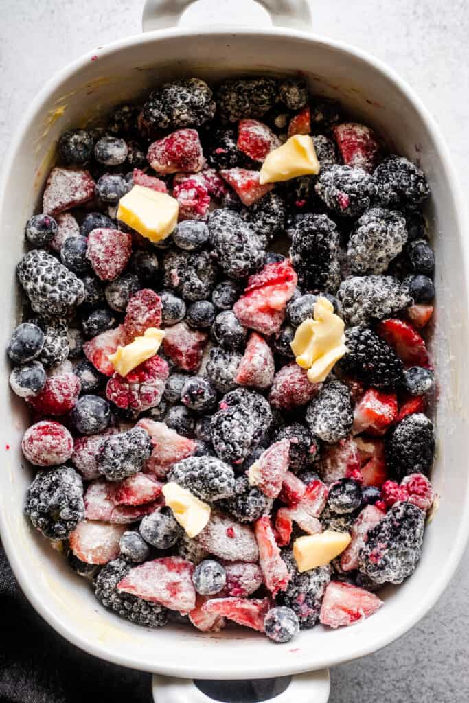 overhead shot of a white baking dish filled with raspberries, strawberries, blackberries, and blueberries that were mixed with flour, sugar, and dotted with chunks of butter.