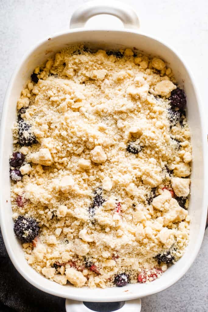a white baking dish with berries topped with a crumbly biscuit topping.