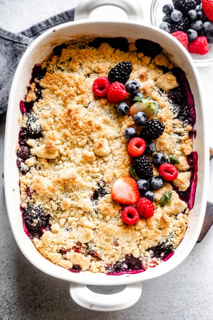 overhead shot of a berry cobbler topped with biscuit topping, plus mixed berries arranged from top to bottom on the right hand side of the cobbler.