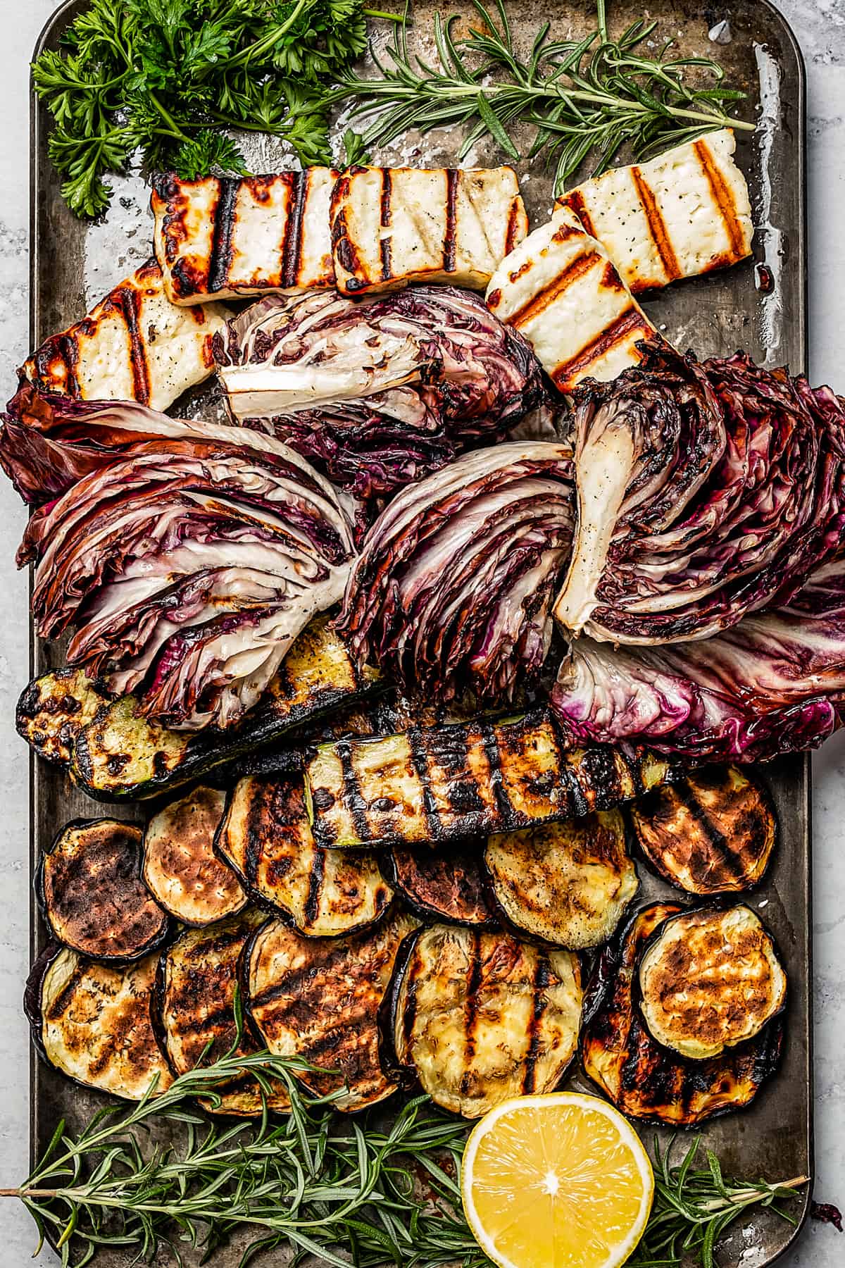 Grilled halloumi cheese, veggies, and garnishes on a sheet pan.