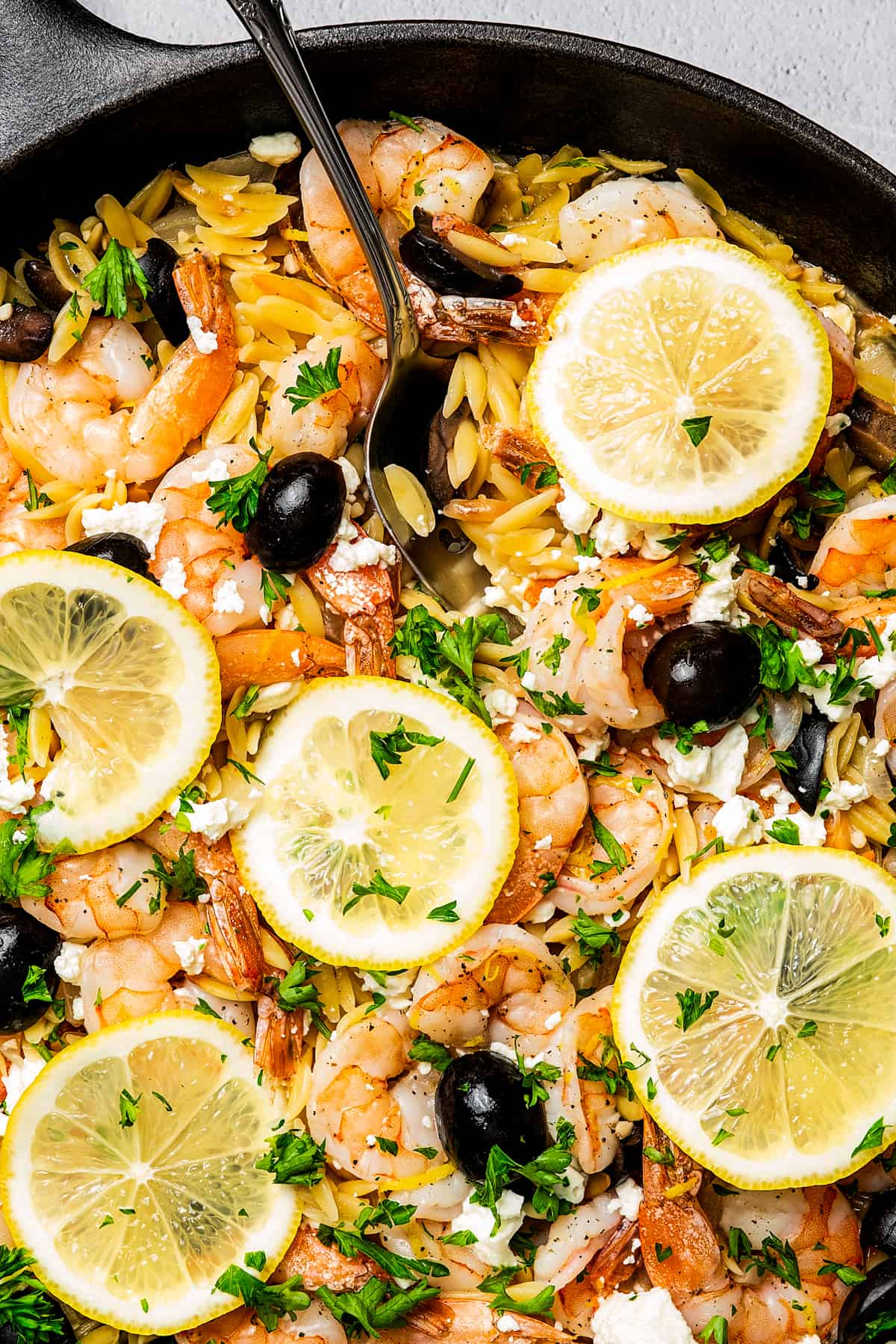 Close-up shot of lemon slices, cooked shrimp, and black olives on a bed of orzo.