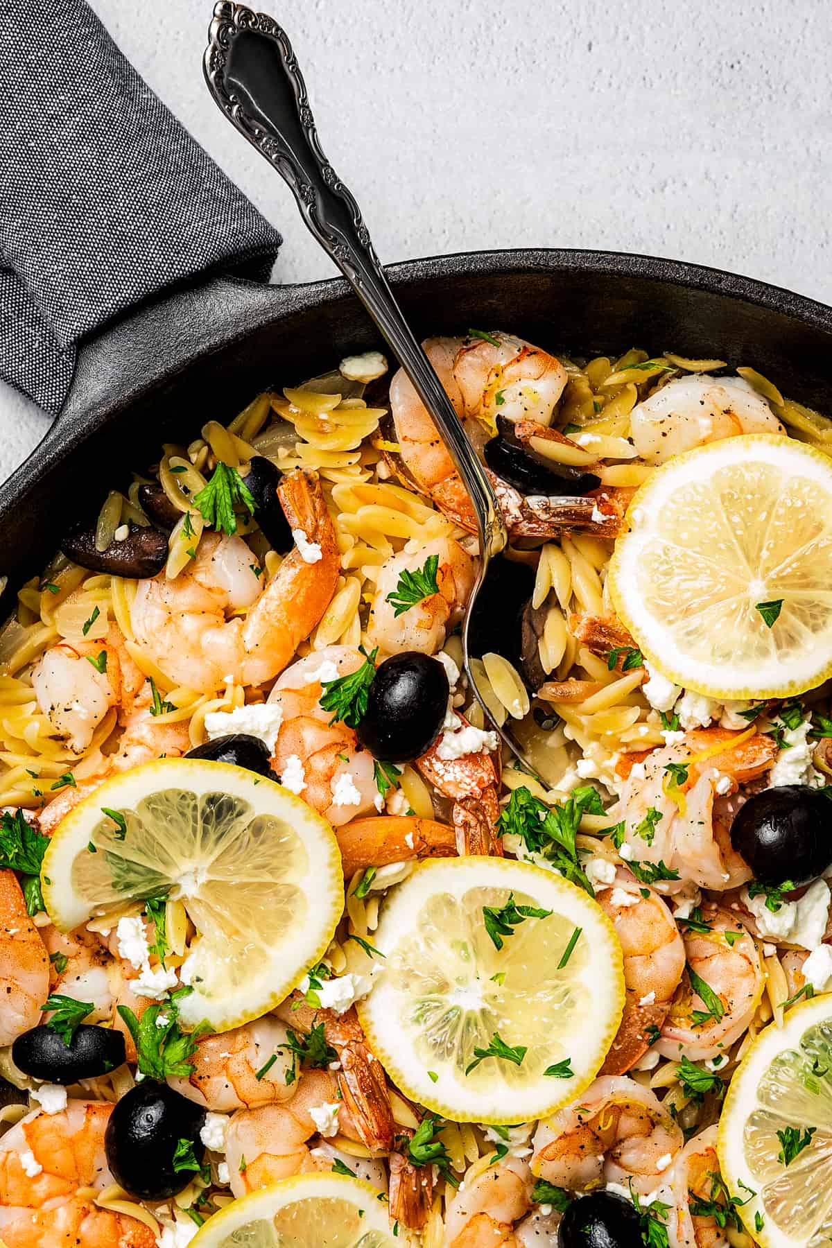 Orzo with seafood and black olives, garnished with lemon and herbs.