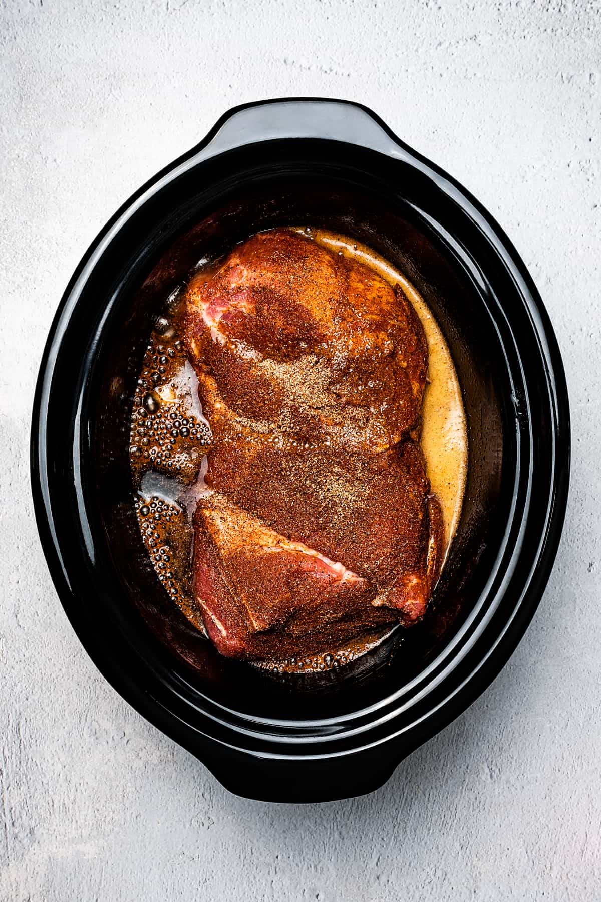 Fully-cooked pork shoulder in a slow cooker insert.