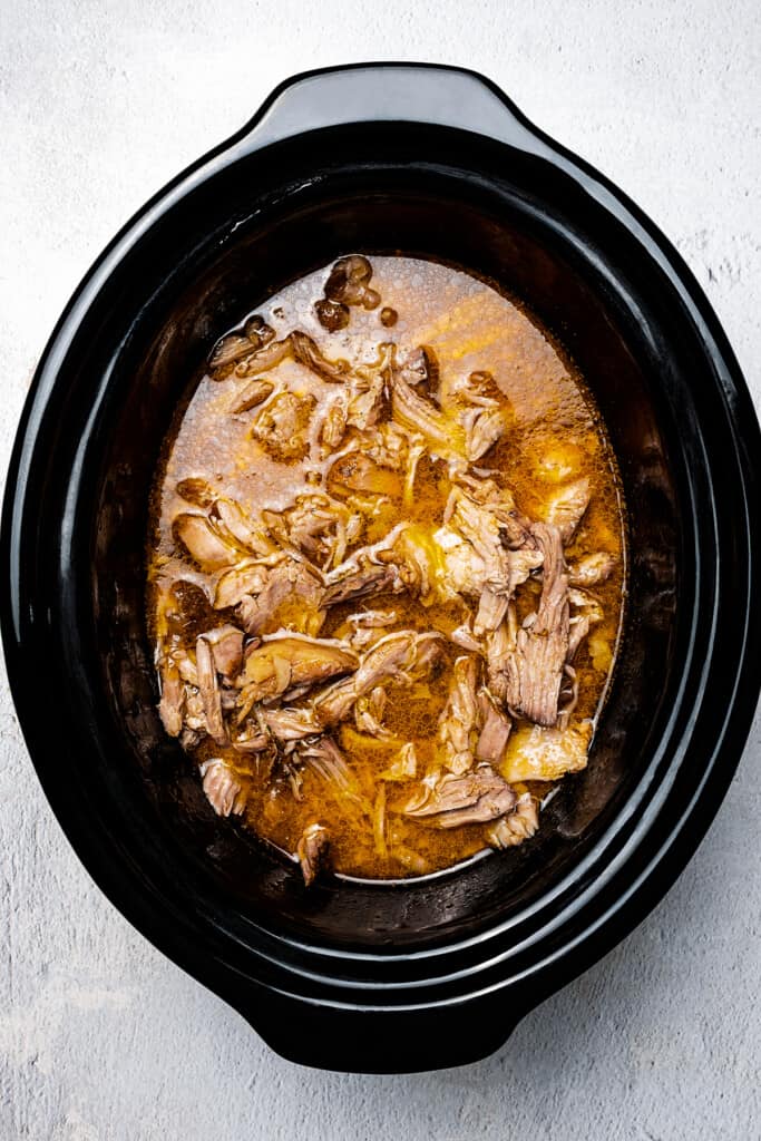 Shredded pork and cooking juices in a crock pot.