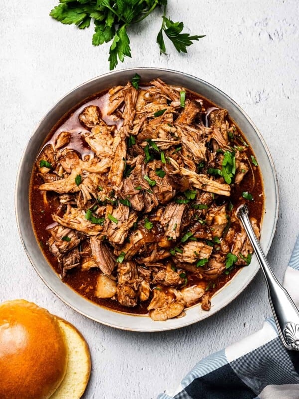 overhead shot of slow cooked pulled pork in a bowl, with burger buns placed to the bottom left of the bowl.