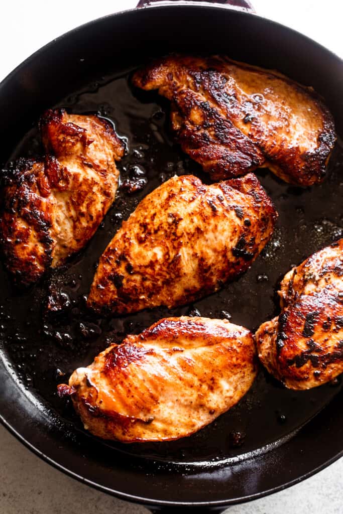 cajun-seasoned chicken breasts cooking in a dark cast iron skillet.