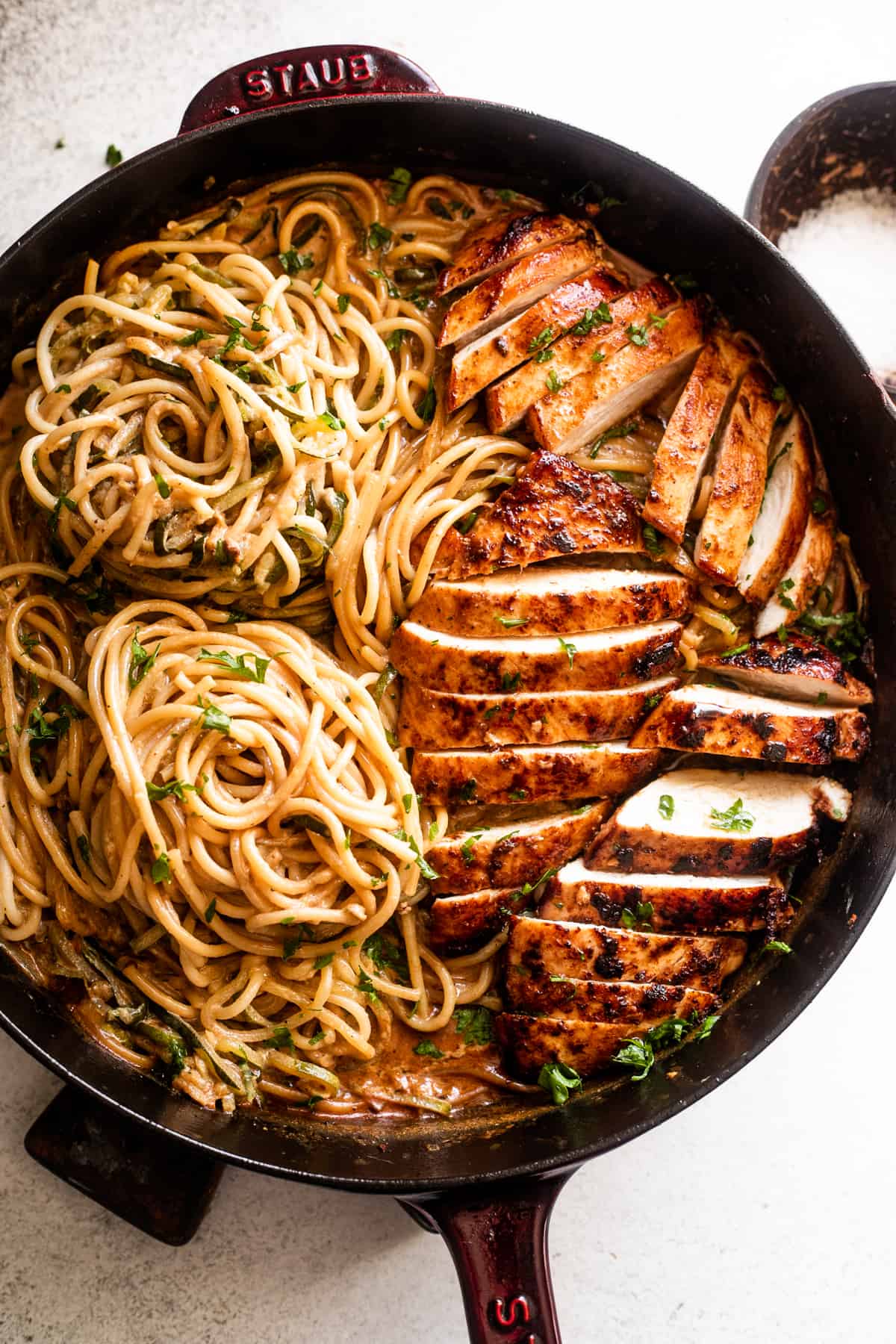 overhead shot of a cast iron skillet with two nests of zoodles arranged on the left side, and sliced chicken breasts arranged on the right side of the skillet.