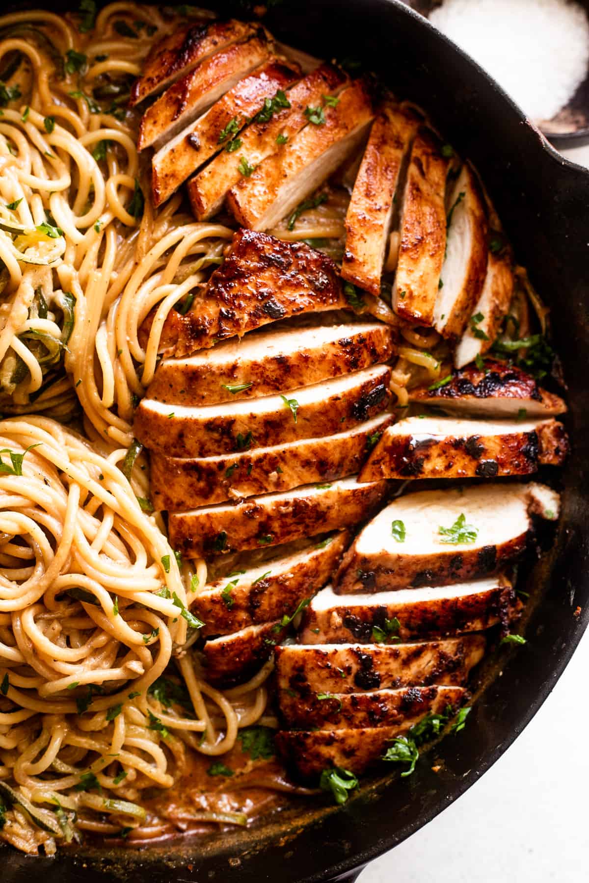 close up shot of a skillet with sliced chicken breasts arranged next to zucchini noodle nests