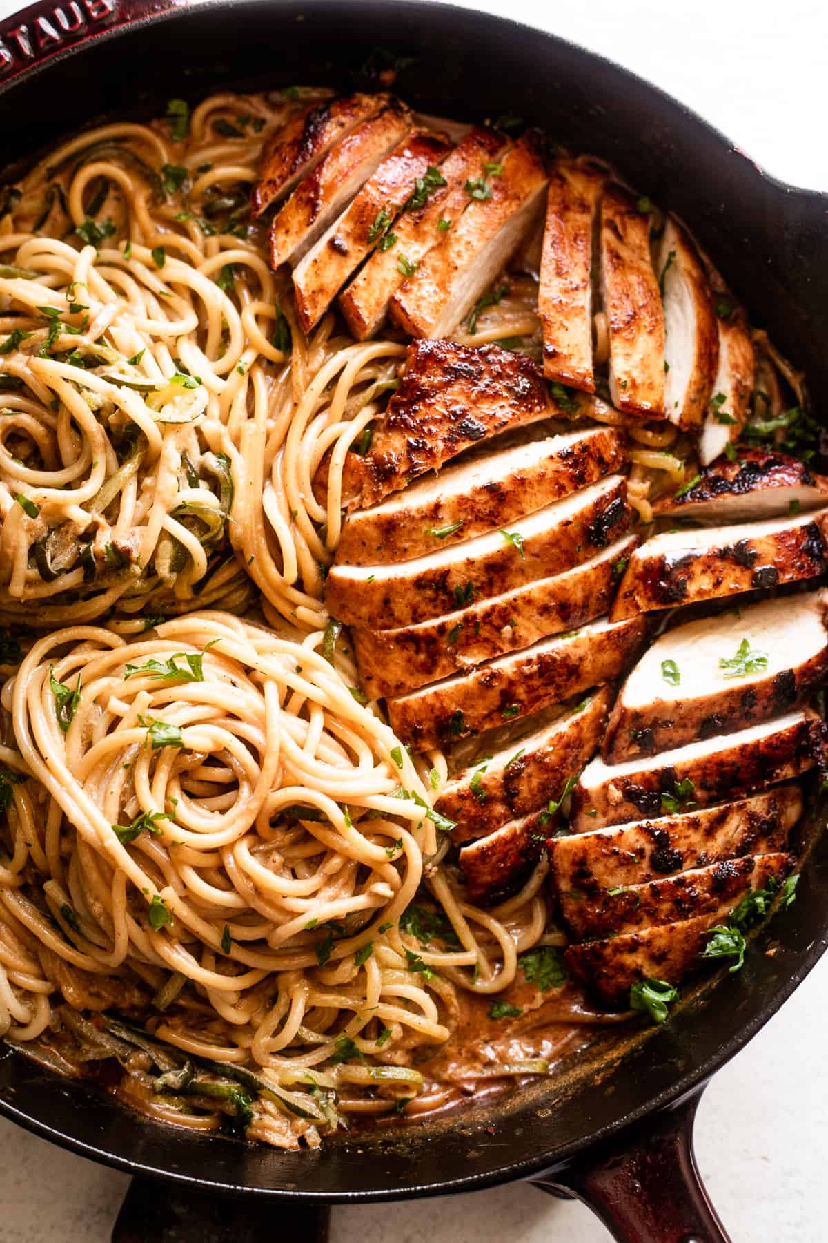 overhead shot of a cast iron skillet with two nests of zoodles arranged on the left side, and sliced chicken breasts arranged on the right side of the skillet.