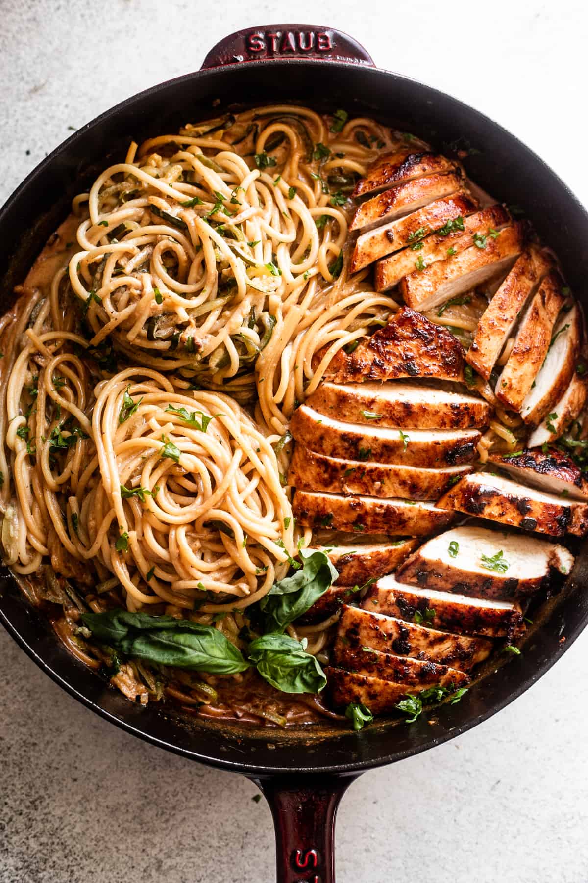 overhead shot of a cast iron skillet with two nests of zoodles arranged on the left side, and sliced chicken breasts arranged on the right side of the skillet.