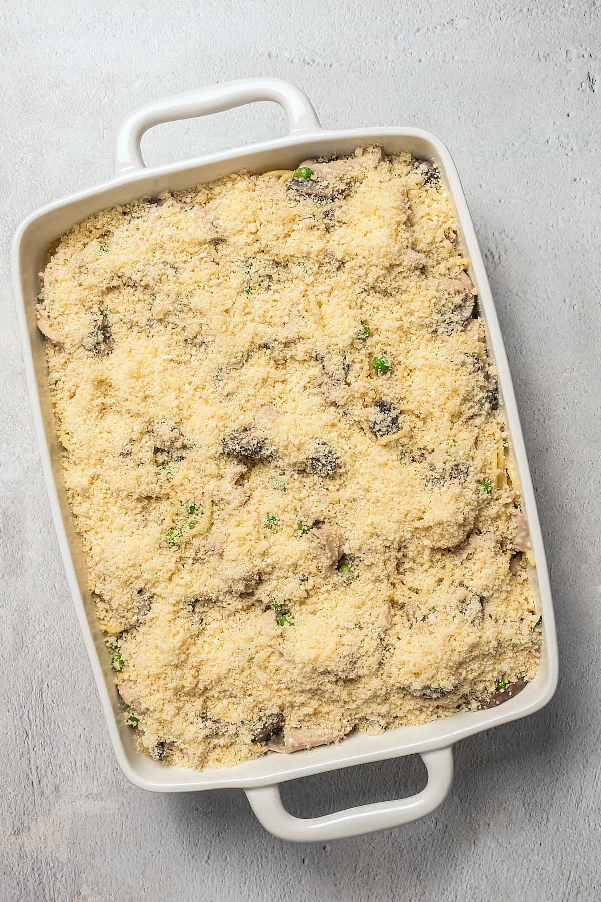 A rectangular dish of unbaked pasta topped with cheese.