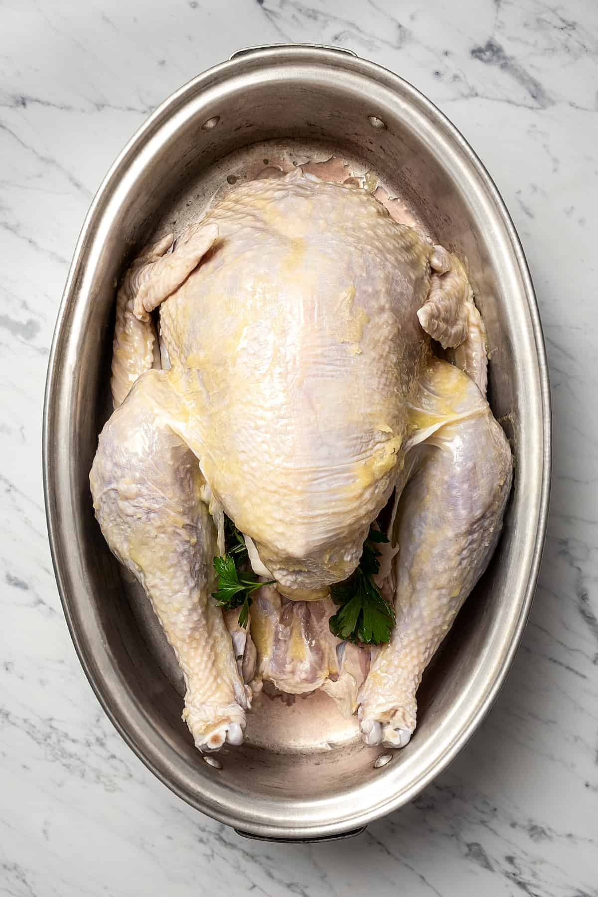 A whole turkey in a roasting pan, with aromatics in the cavity and butter brushed all over, ready for roasting.